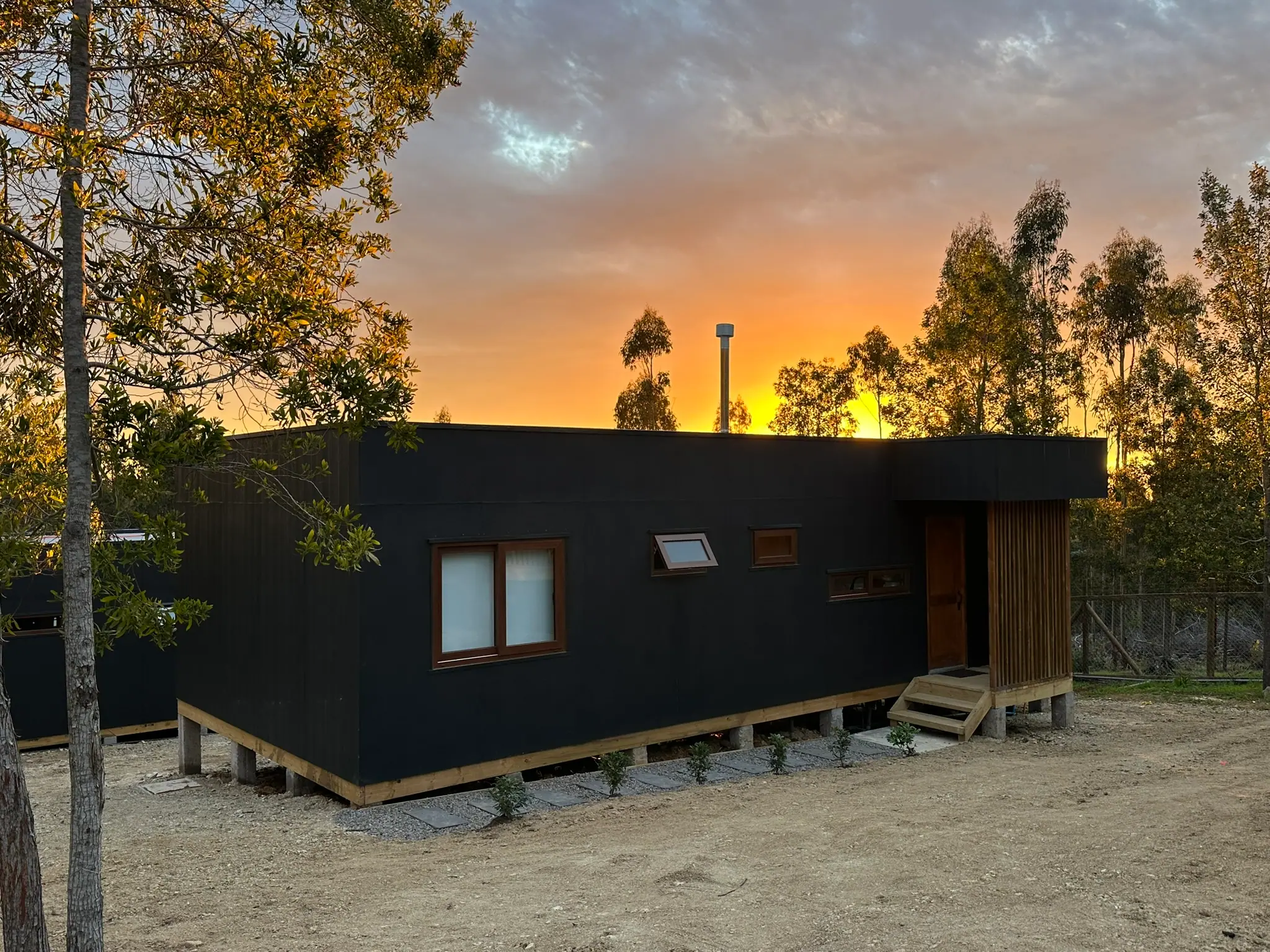 Cabaña de Bush Lodge al atardecer, con el cielo naranjo entre los árboles